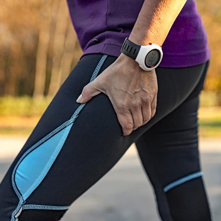 A person holding their upper thigh. They are wearing leggings.